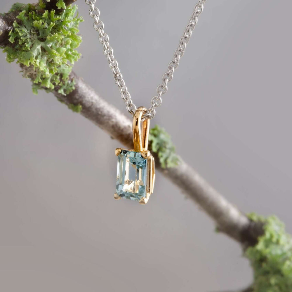 10kt yellow gold emerald cut aquamarine pendant on a silver chain, hanging from a branch
