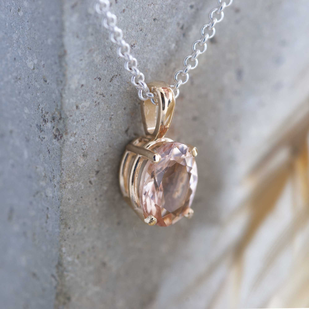 10kt yellow gold pendant with oval peach morganite on a silver chain, shown against stone