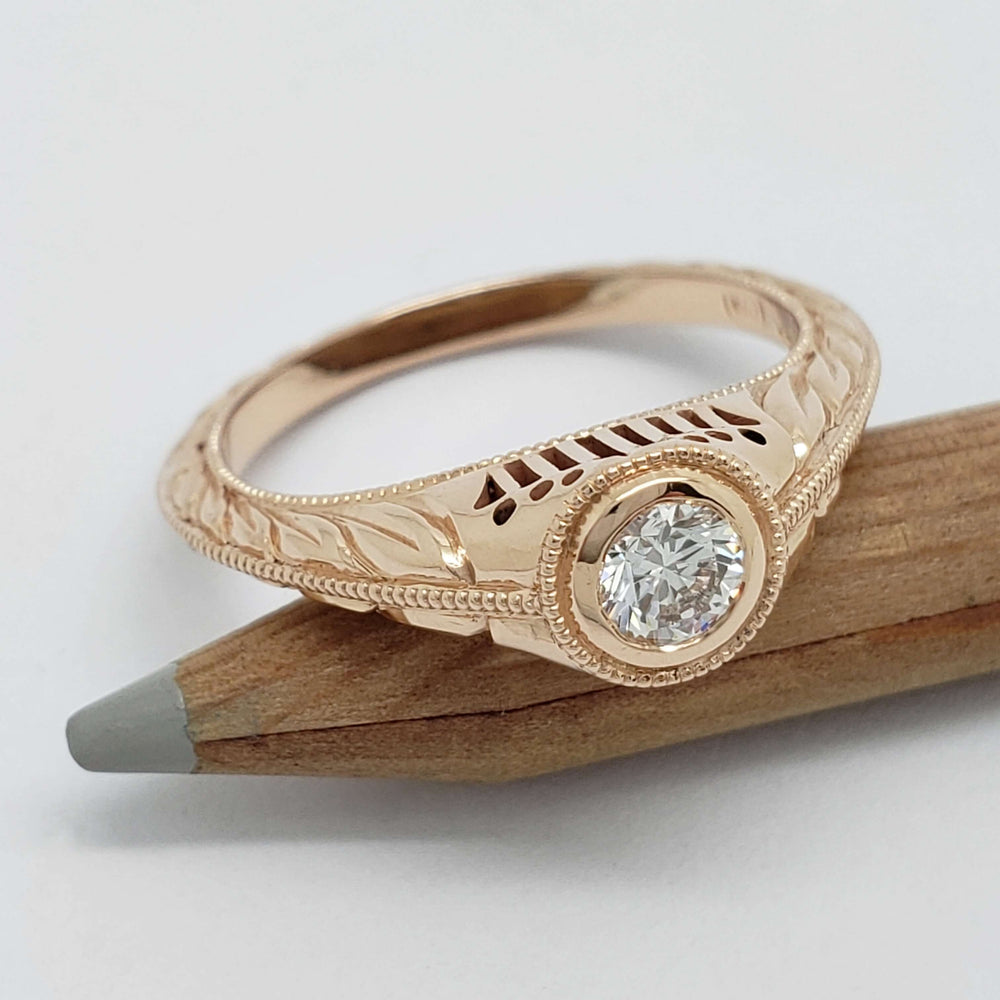 14k rose gold bezel set diamond ring with filigree, hand engraving and millgrain on a pencil