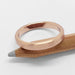 14k rose gold flat wedding band with brushed finish resting on a pencil