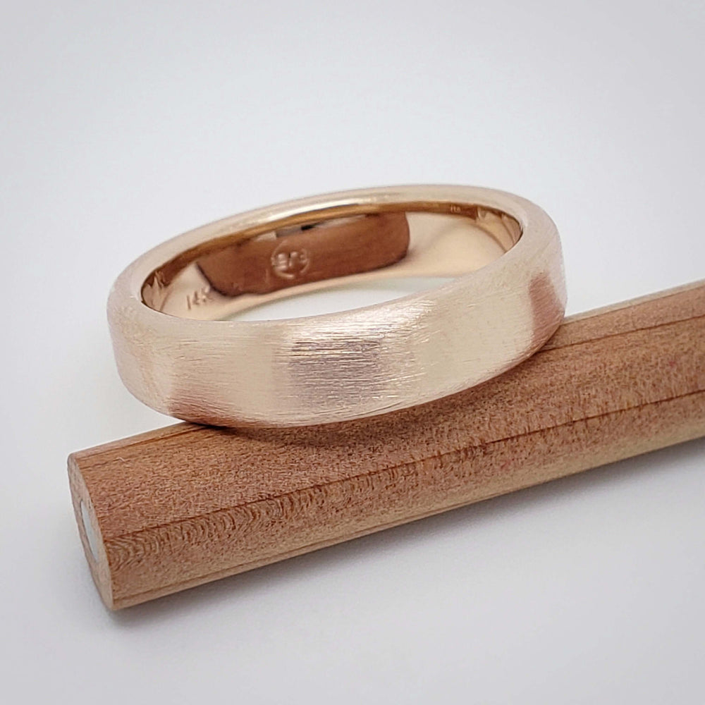 14k rose gold flat wedding band with brushed finish resting on wood