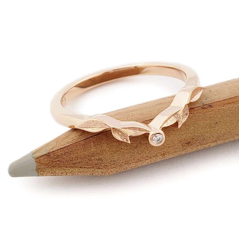 14k rose gold leaf wedding ring with diamond, displayed on a wooden pencil