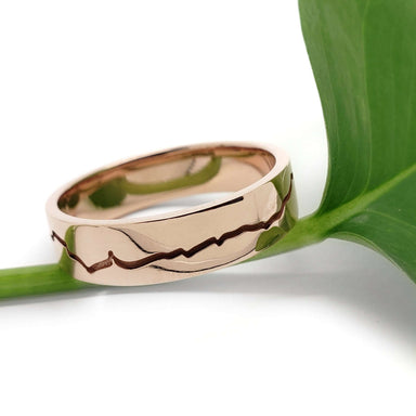 14k rose gold mountain range wedding ring resting on a green leaf, polished finish
