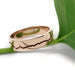 14k rose gold mountain range wedding ring resting on a green leaf, polished finish