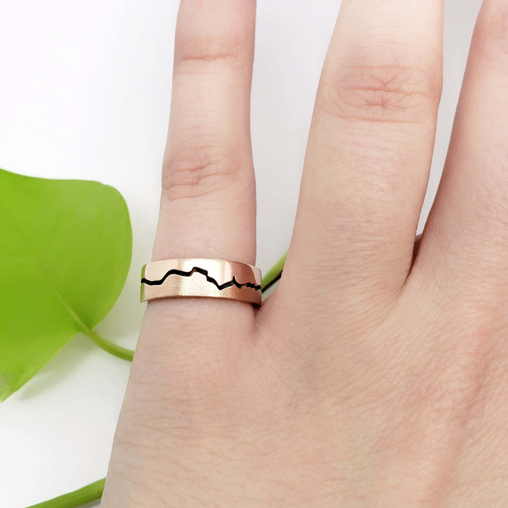 14k rose gold mountain range wedding ring with blackened detail, shown on hand