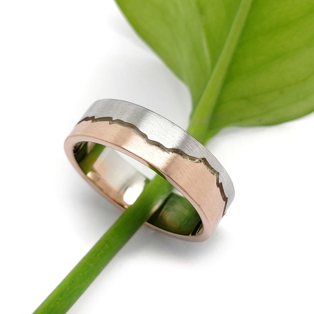 14k white and rose gold mountain range wedding ring resting on a green leaf