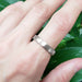 14k white gold brushed wedding ring worn on a hand with green leaves in background