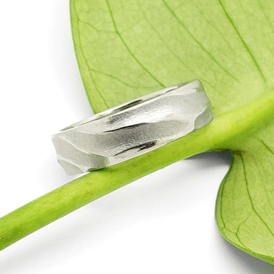 14k white gold textured wedding ring with topography pattern resting on a green leaf