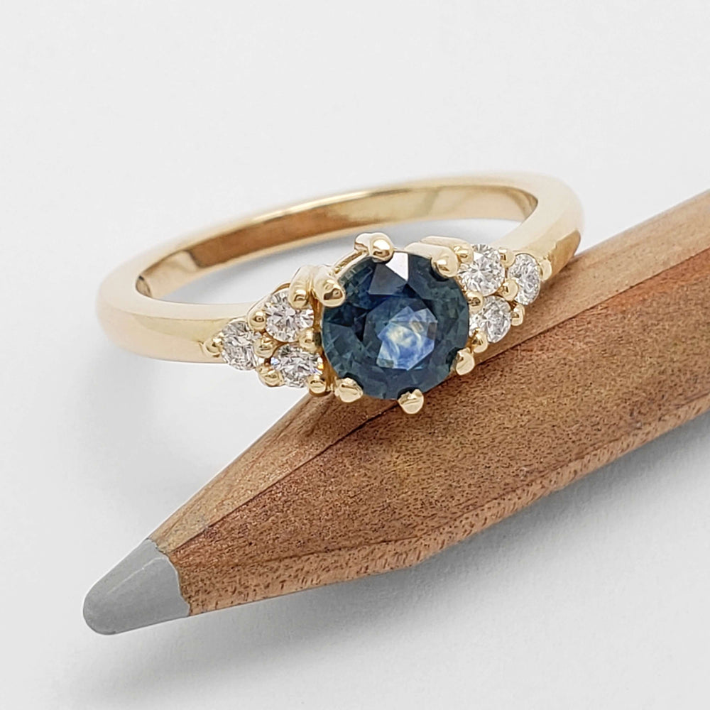 Montana sapphire and diamond 14k yellow gold ring resting on a pencil, top view