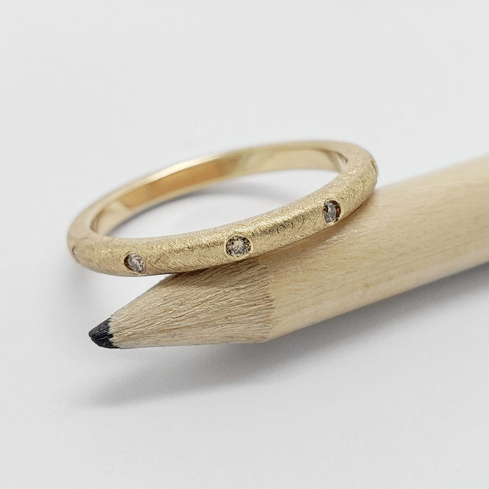 14k yellow gold champagne diamond band resting on a pencil