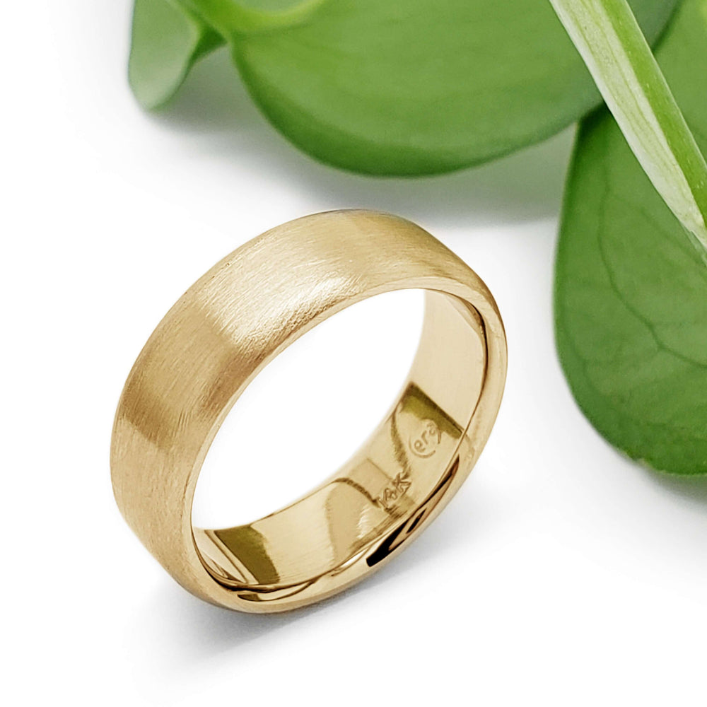 14k yellow gold flat wedding ring with brushed finish beside green leaves