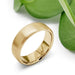 14k yellow gold flat wedding ring with brushed finish beside green leaves