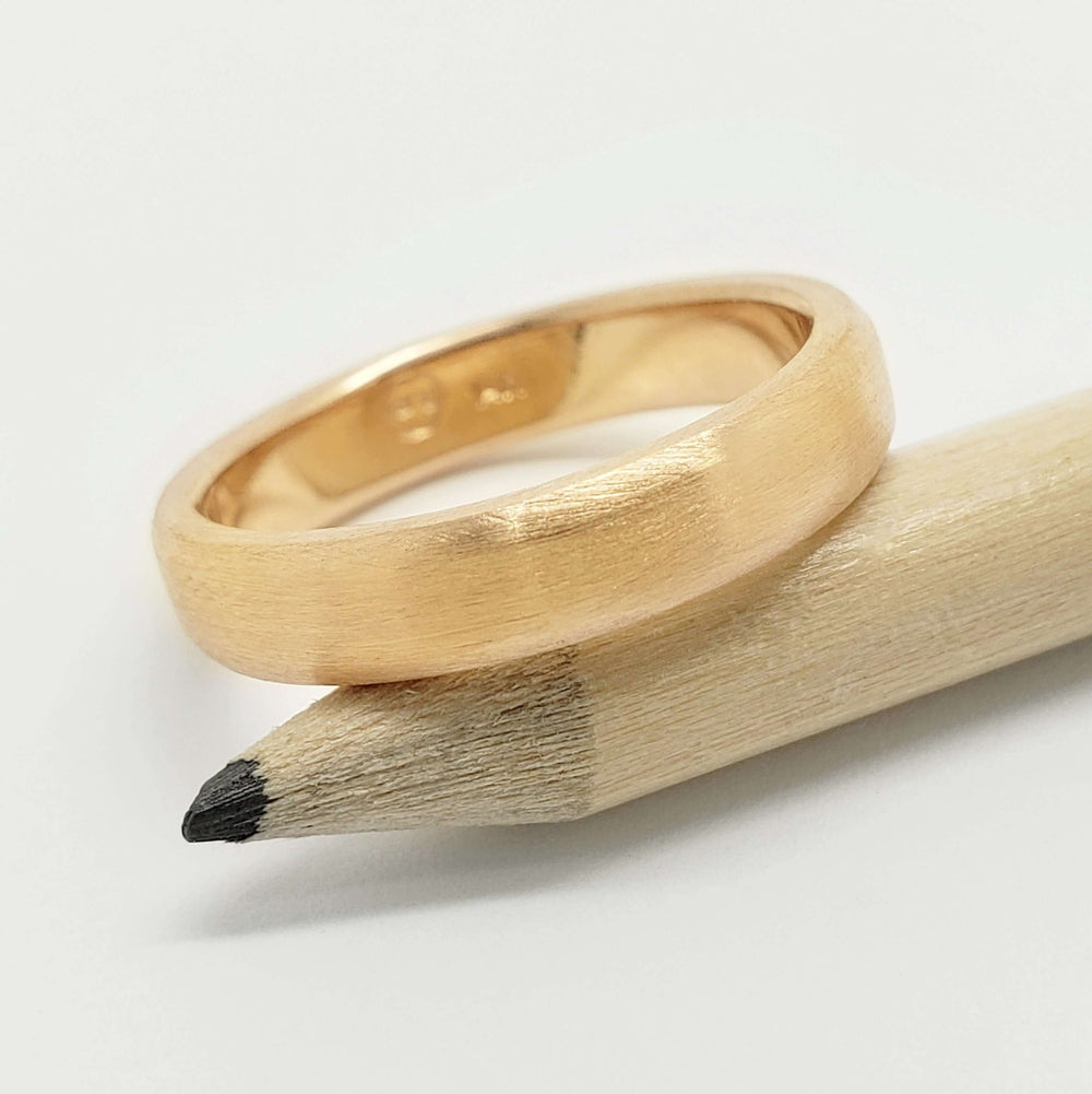 14k yellow gold flat wedding ring with brushed finish displayed on a pencil