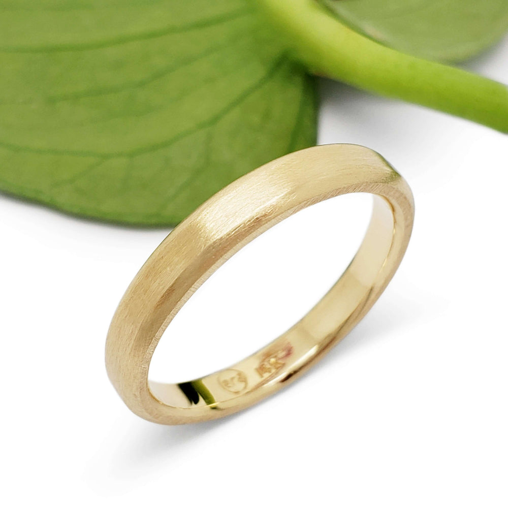 14k yellow gold flat wedding ring with brushed texture beside a green leaf