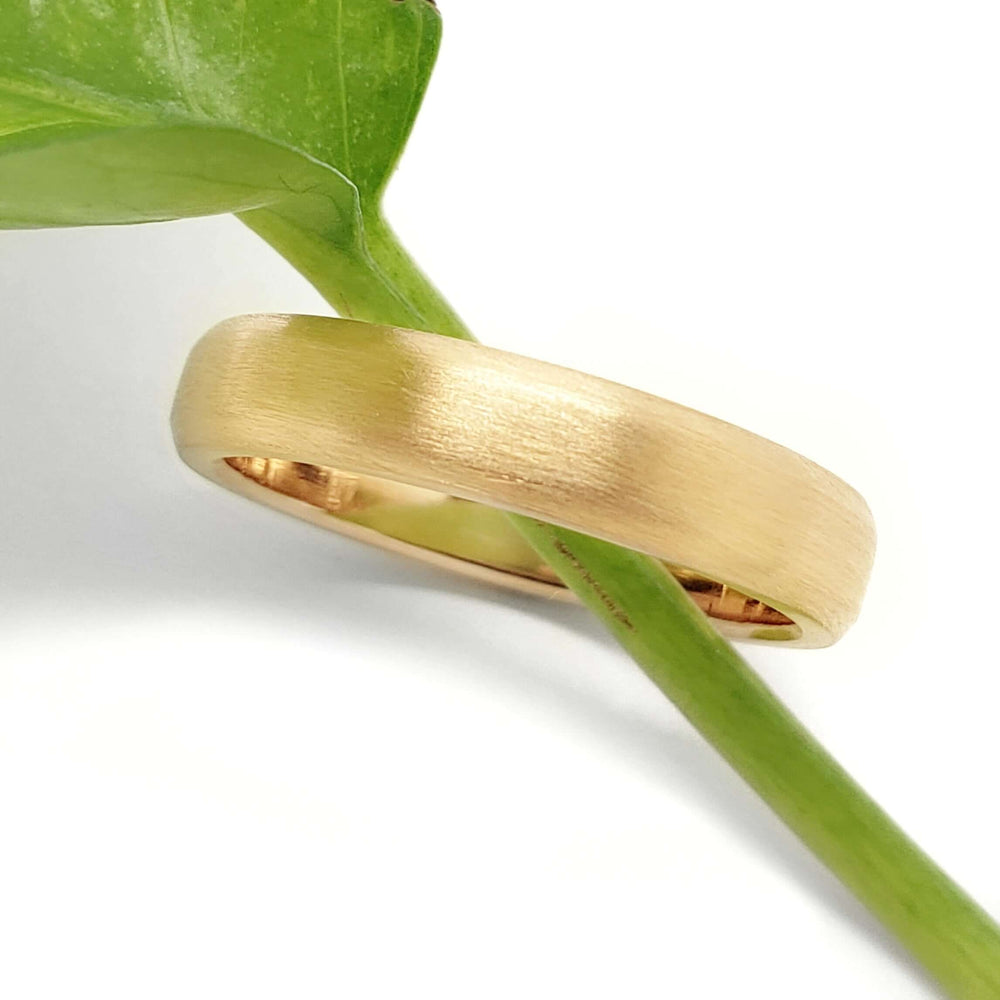 14k yellow gold flat wedding ring with brushed texture resting on a green leaf