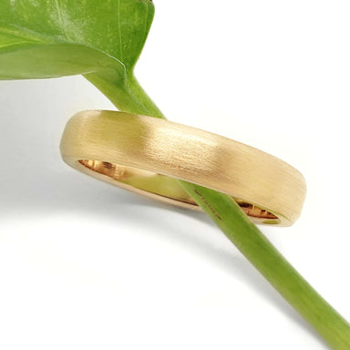14k yellow gold flat wedding ring with brushed texture resting on a green leaf