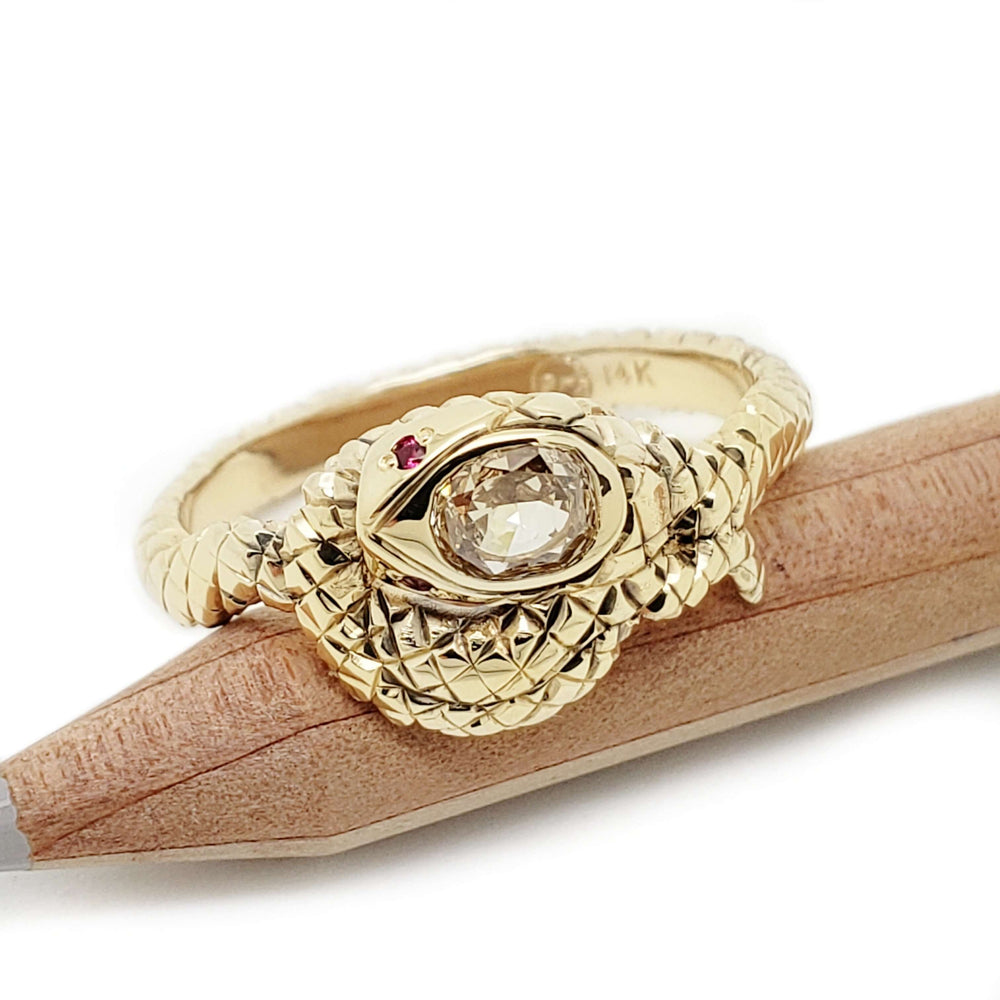 14k yellow gold snake ring with champagne diamond and ruby eyes, resting on pencil