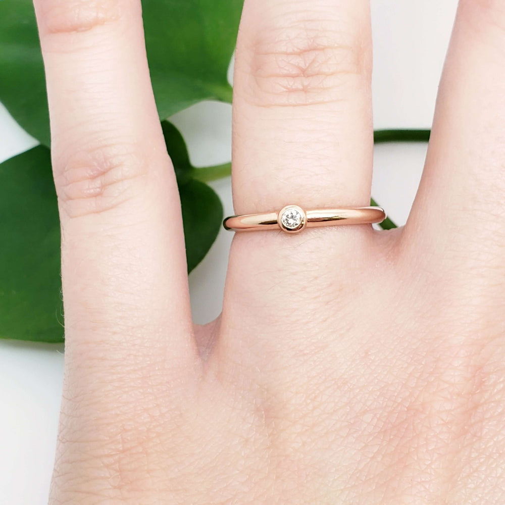 14kt rose gold bezel set diamond ring worn on a hand with green leaf background