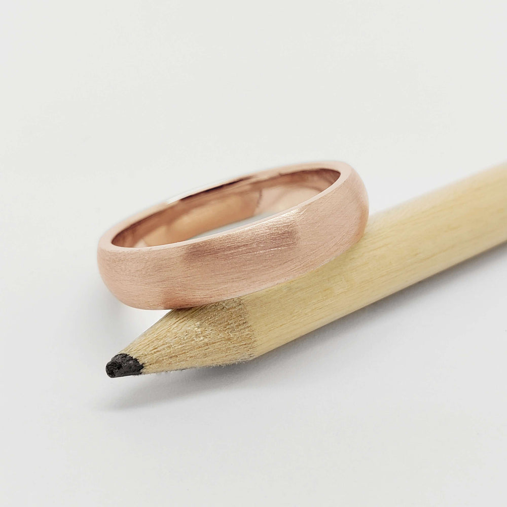 14kt rose gold brushed wedding ring resting on a pencil