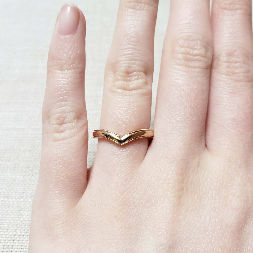14kt rose gold chevron wedding ring with millgrain, worn on a hand