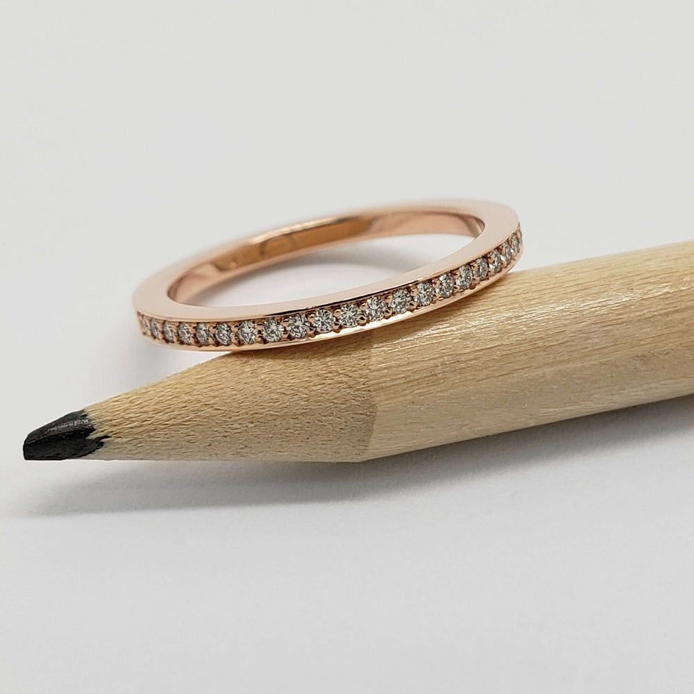 14kt rose gold diamond pave wedding ring resting on a pencil