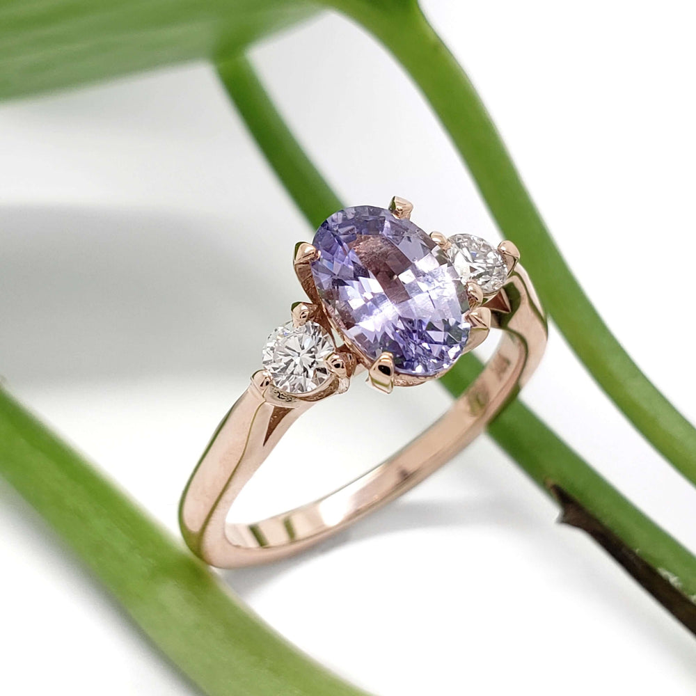 14kt rose gold engagement ring with purple sapphire and lab-grown diamonds beside green leaves