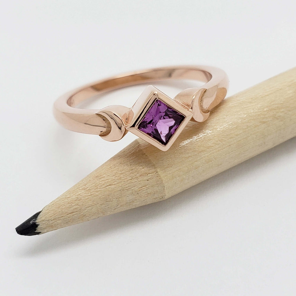 14kt rose gold engagement ring with purple sapphire, displayed on a pencil