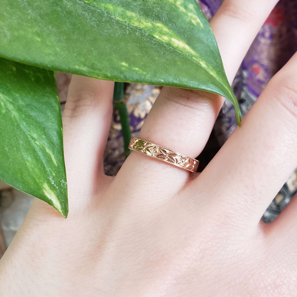 14kt rose gold floral engraved wedding ring shown on a hand