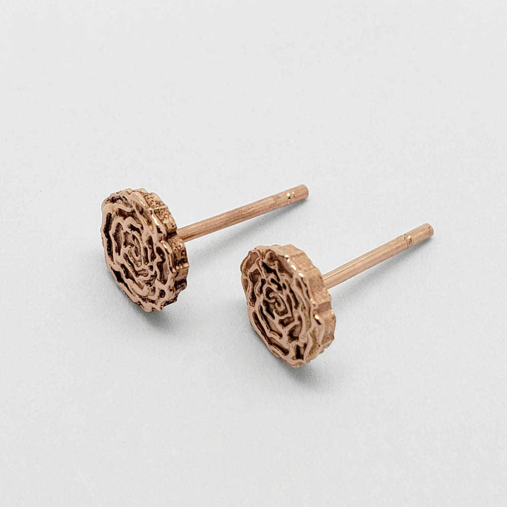 Side angle of 14kt rose gold floral rose stud earrings on white surface