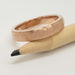 14kt rose gold hammered wedding band resting on a pencil