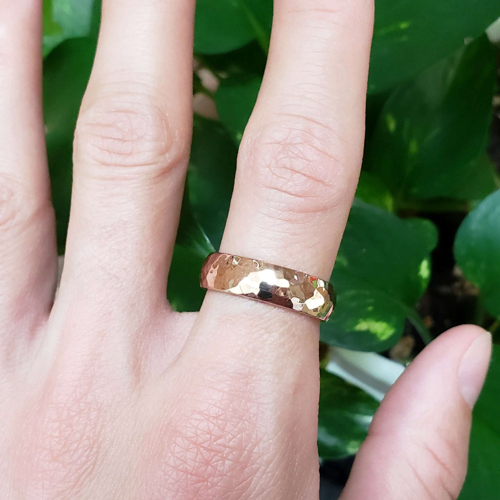 14kt rose gold hammered wedding ring worn on a hand, showing polished texture
