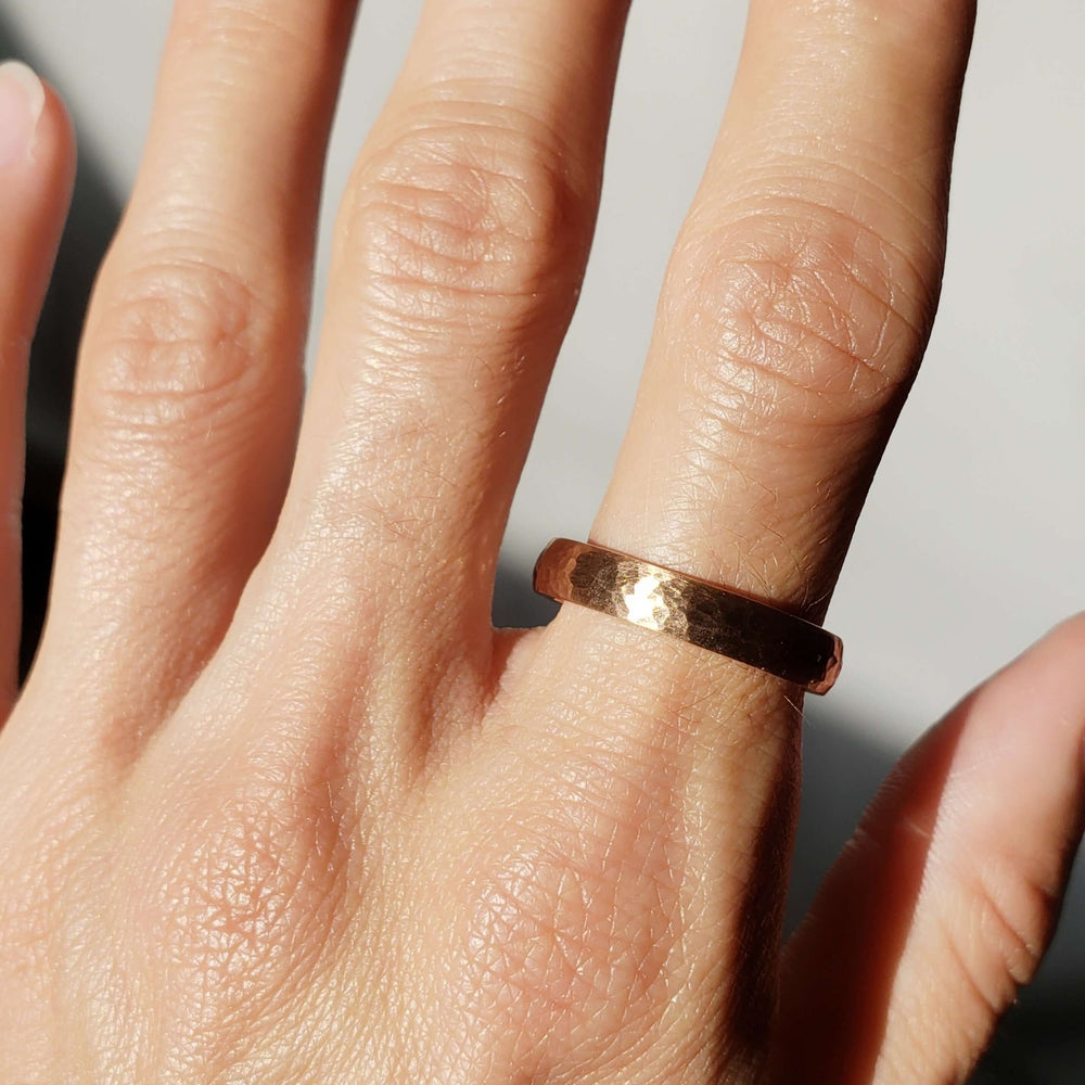 14kt rose gold hammered wedding ring shown on a hand