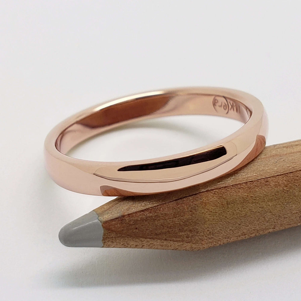 14kt rose gold low dome wedding band resting on a pencil
