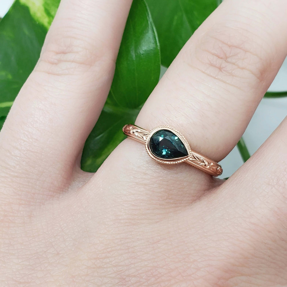 14kt rose gold teal sapphire engagement ring with engraving, worn on hand