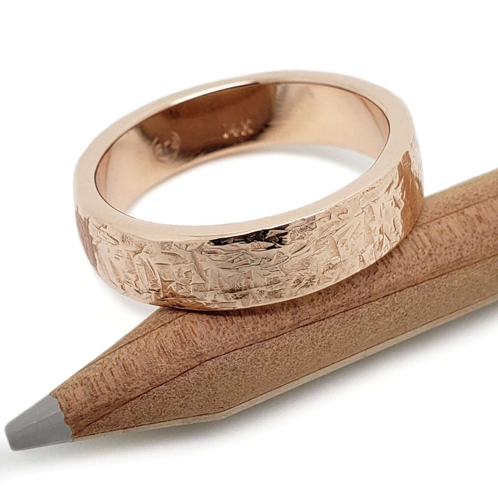 14kt rose gold textured wedding band resting on a pencil, showing artisan detail