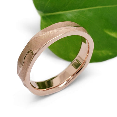 14kt rose gold textured wedding ring beside a green leaf