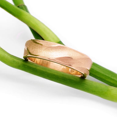 14kt rose gold textured wedding ring displayed on green plant stems