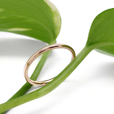 14kt rose gold wedding band displayed on a green leaf