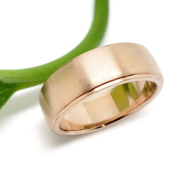 14kt rose gold wedding band with a brushed finish beside a green stem