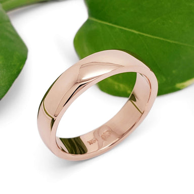 14kt rose gold wedding band with a polished finish, shown beside green leaves