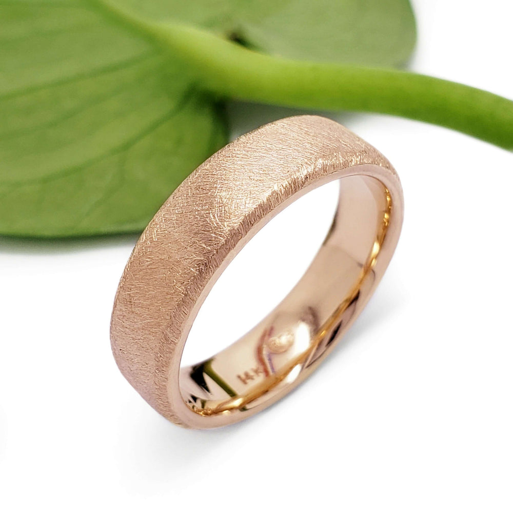 14kt rose gold wedding band with saw blade texture beside a green leaf
