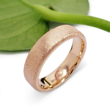 14kt rose gold wedding band with saw blade texture beside a green leaf