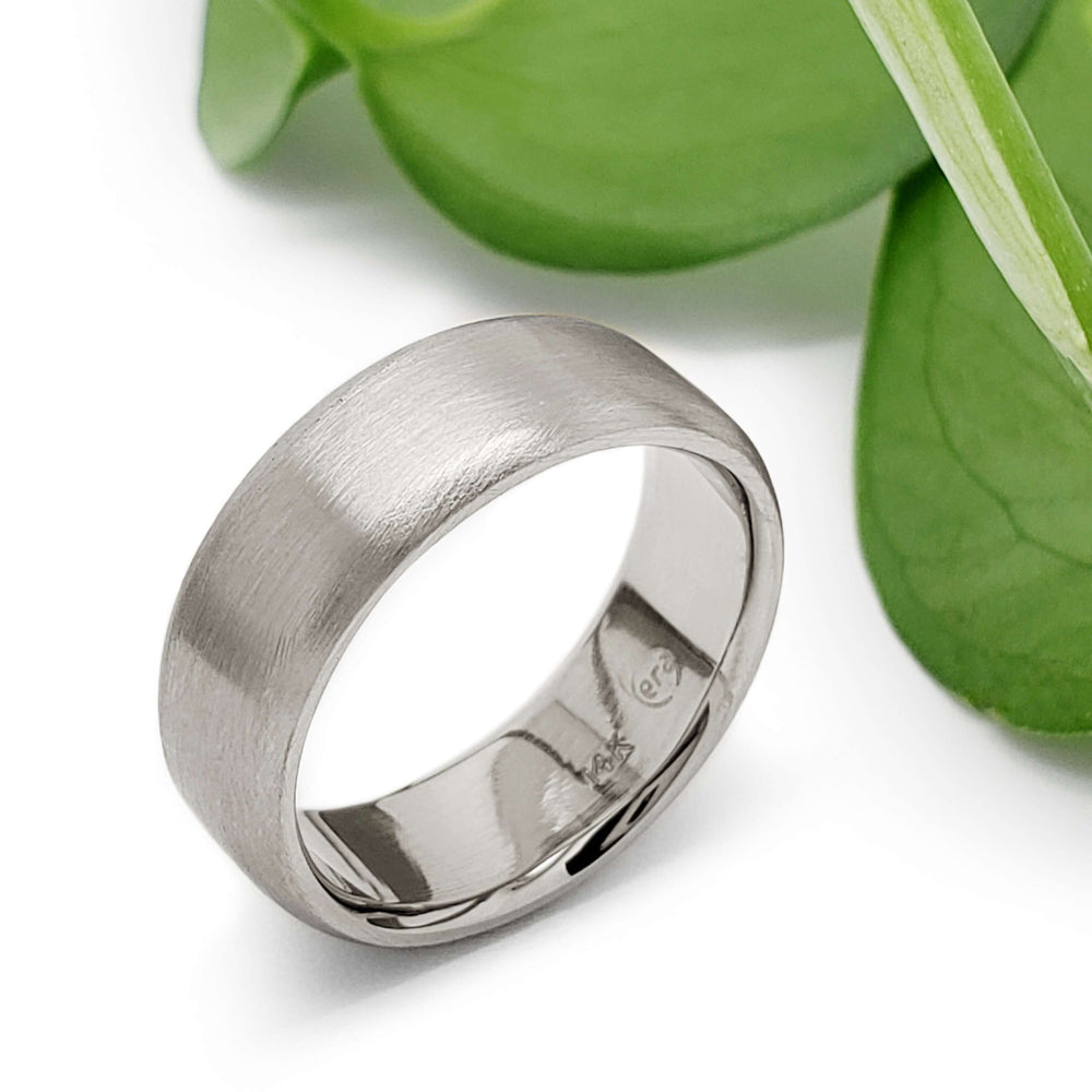 14kt white gold brushed flat wedding band beside green leaves