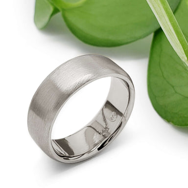 14kt white gold brushed flat wedding band beside green leaves