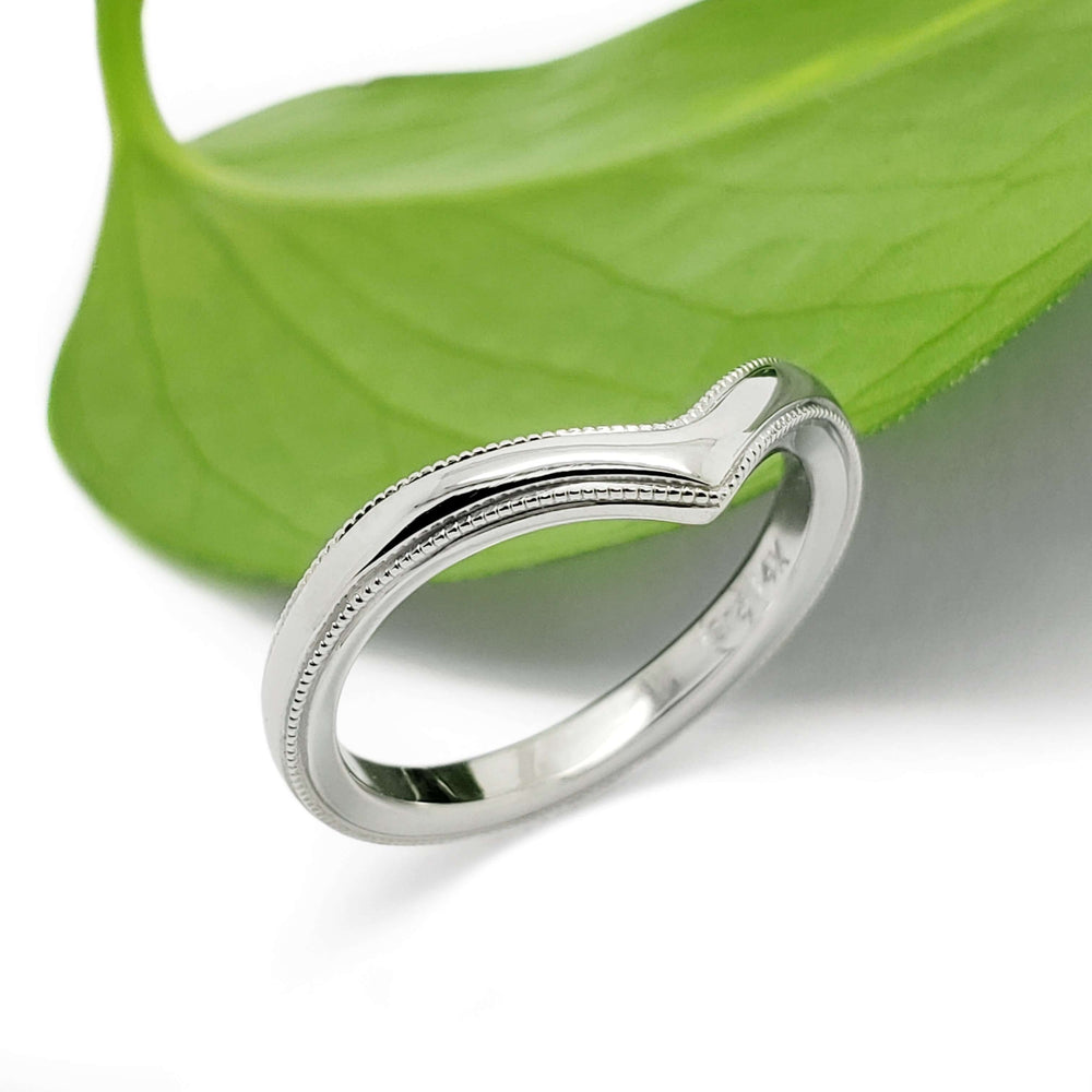14kt white gold chevron millgrain wedding band beside a green leaf