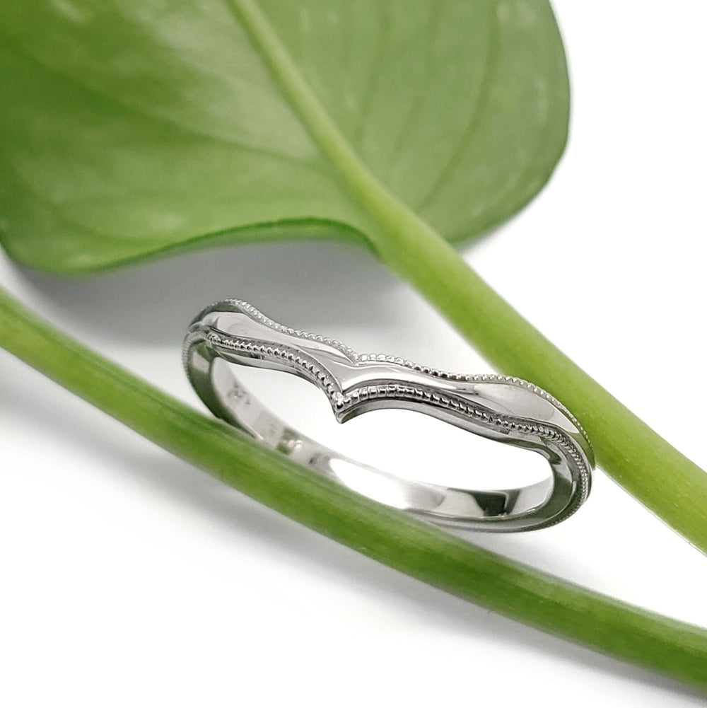 14kt white gold chevron wedding ring with millgrain, displayed on a green plant stem