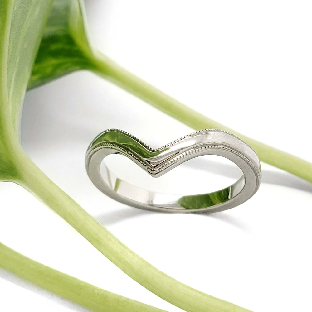 14kt white gold chevron wedding ring with millgrain, displayed on green plant