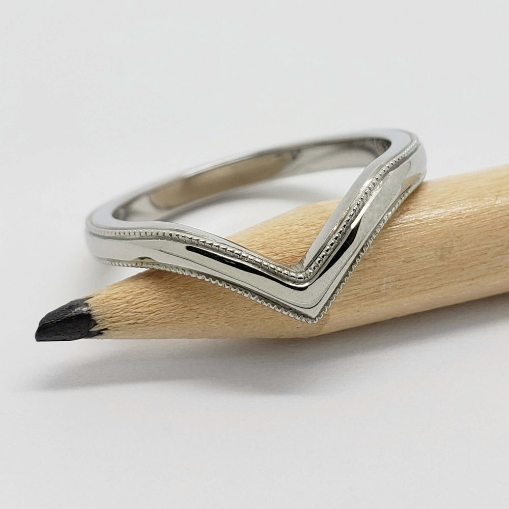 14kt white gold chevron wedding ring with millgrain, resting on a pencil