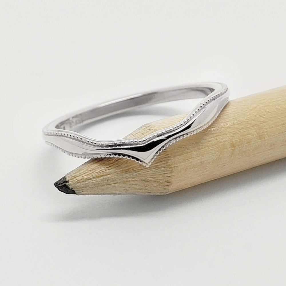 14kt white gold chevron wedding ring with millgrain, resting on a pencil