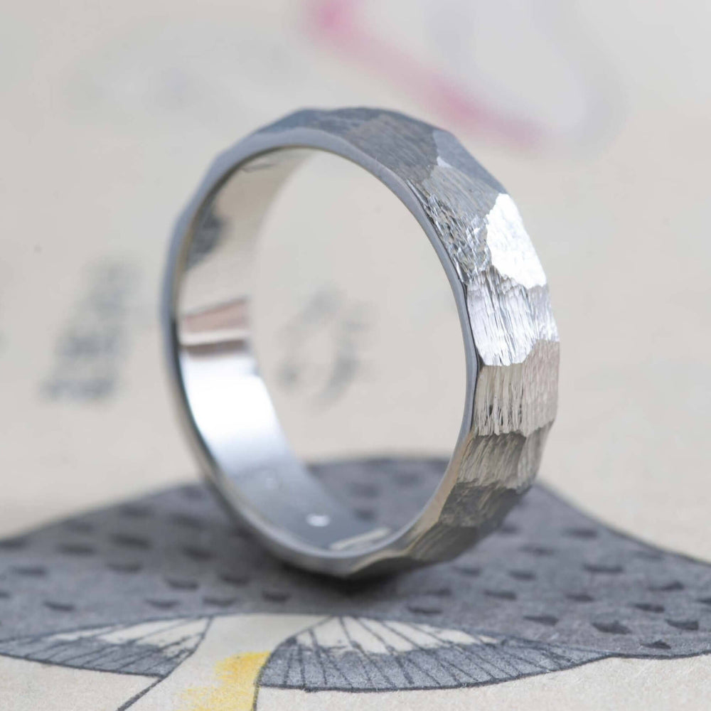 14kt white gold custom carved wedding ring with rough faceted texture, angled on paper